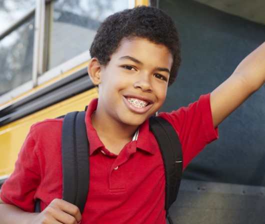 young boy leaning against school bus with braces