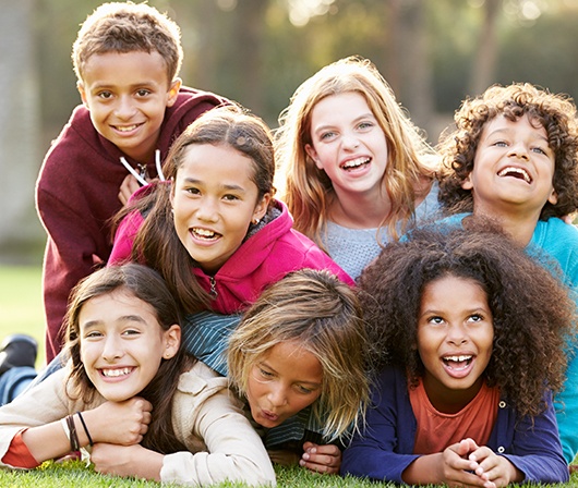 7 children in a pile smiling and laughing on grass