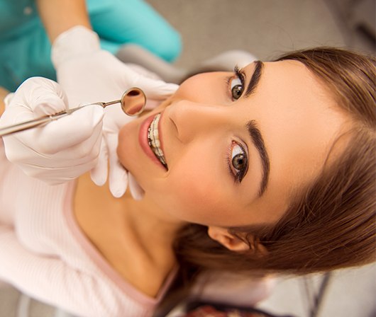 Young woman receiving orthodontic exam smiling up at camera