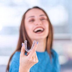 Laughing woman holding aligner for Invisalign in Dallas, TX