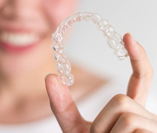A young woman holding a clear Invisalign aligner in her hand and smiling