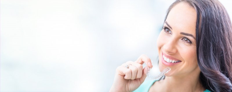 a middle-aged woman with dark hair holding an Invisalign aligner in her right hand