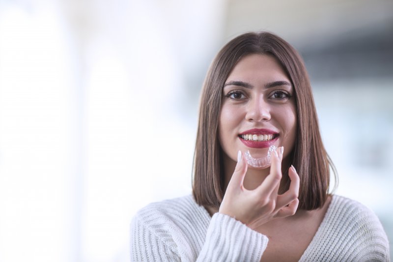 a woman holding her Invisalign aligner and preparing to insert it into her mouth