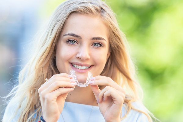 woman smiling holding Invisalign aligner