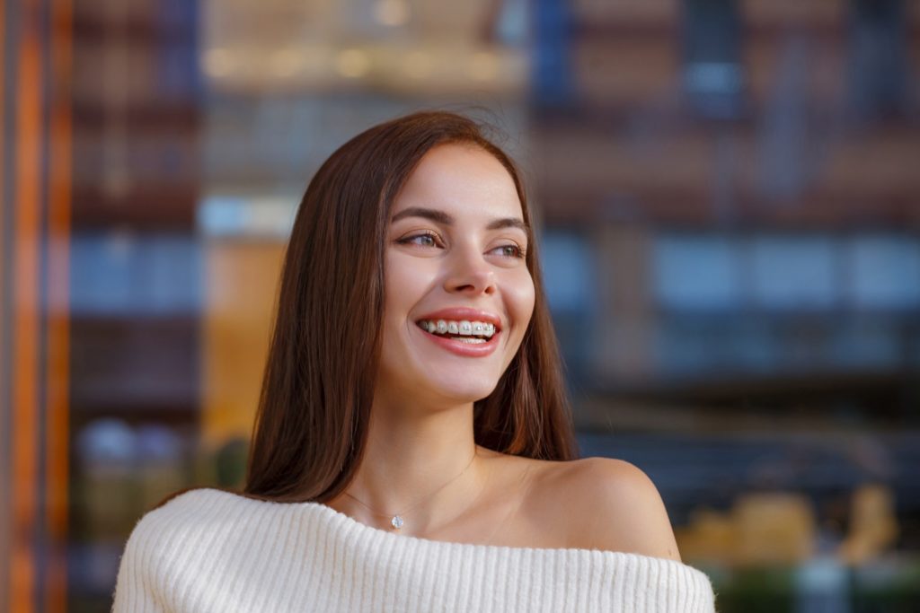 Woman in cream sweater smiling with braces